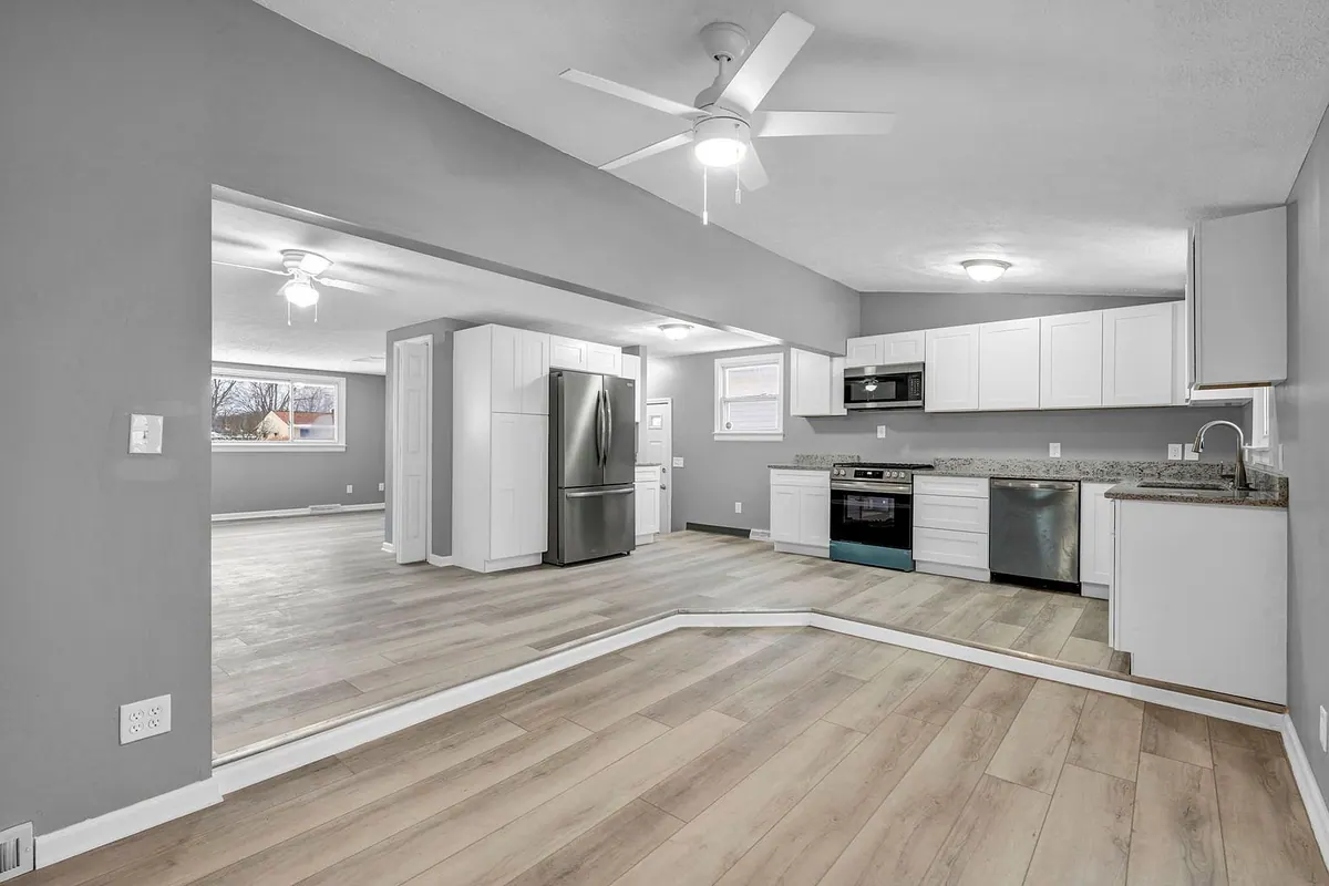 Kitchen with white cabinets, granite counters and a gas range, open through to the living room