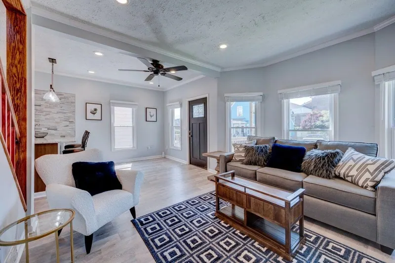 Living room with a gray sofa, patterned rug and windows along two walls